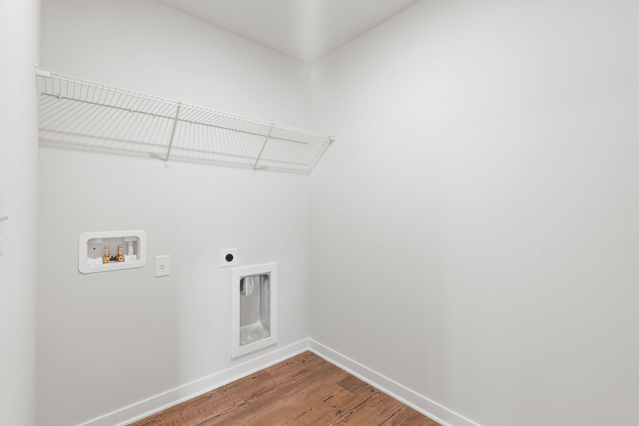 A room with a wood floor and a white wall with a vent.