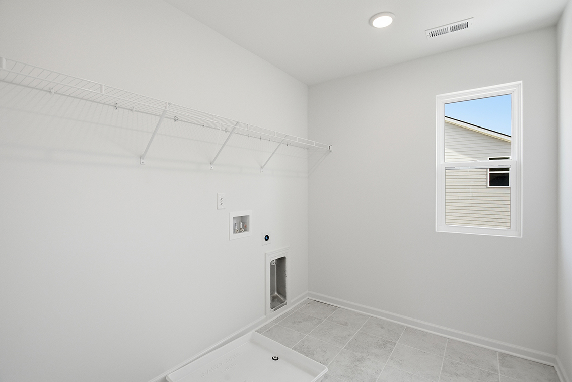 A white tiled room with a bathtub and a window.