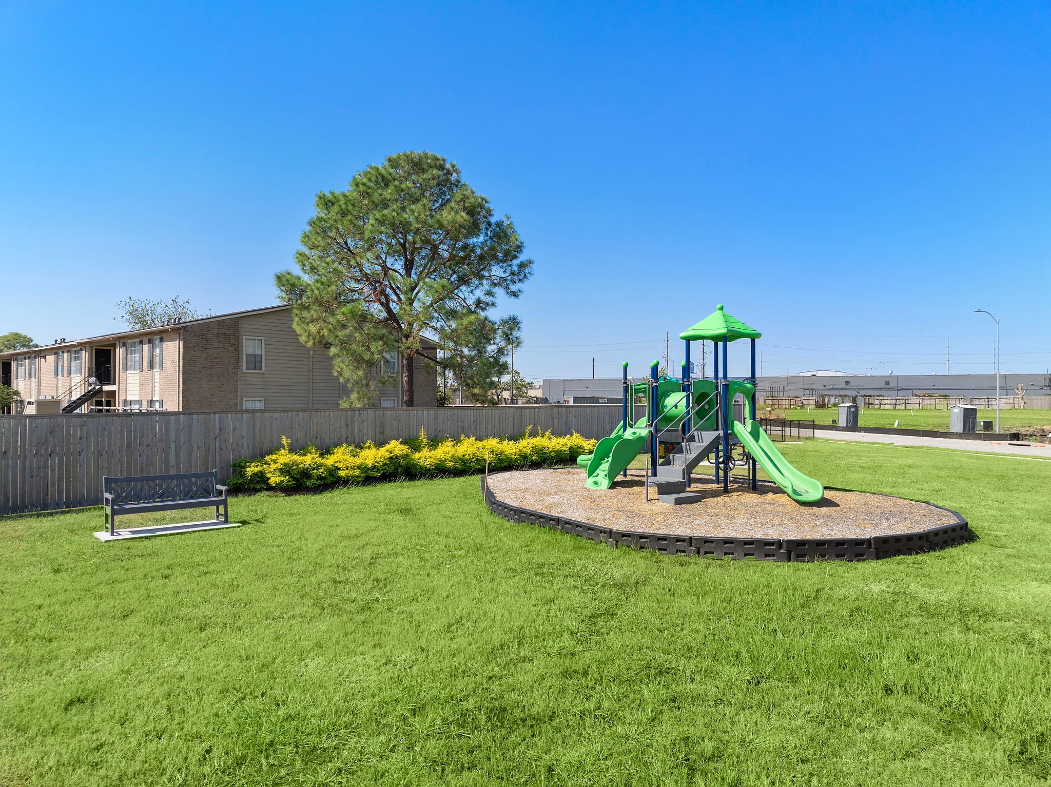 A small play structure in a grassy area with a tree and a building in the background.