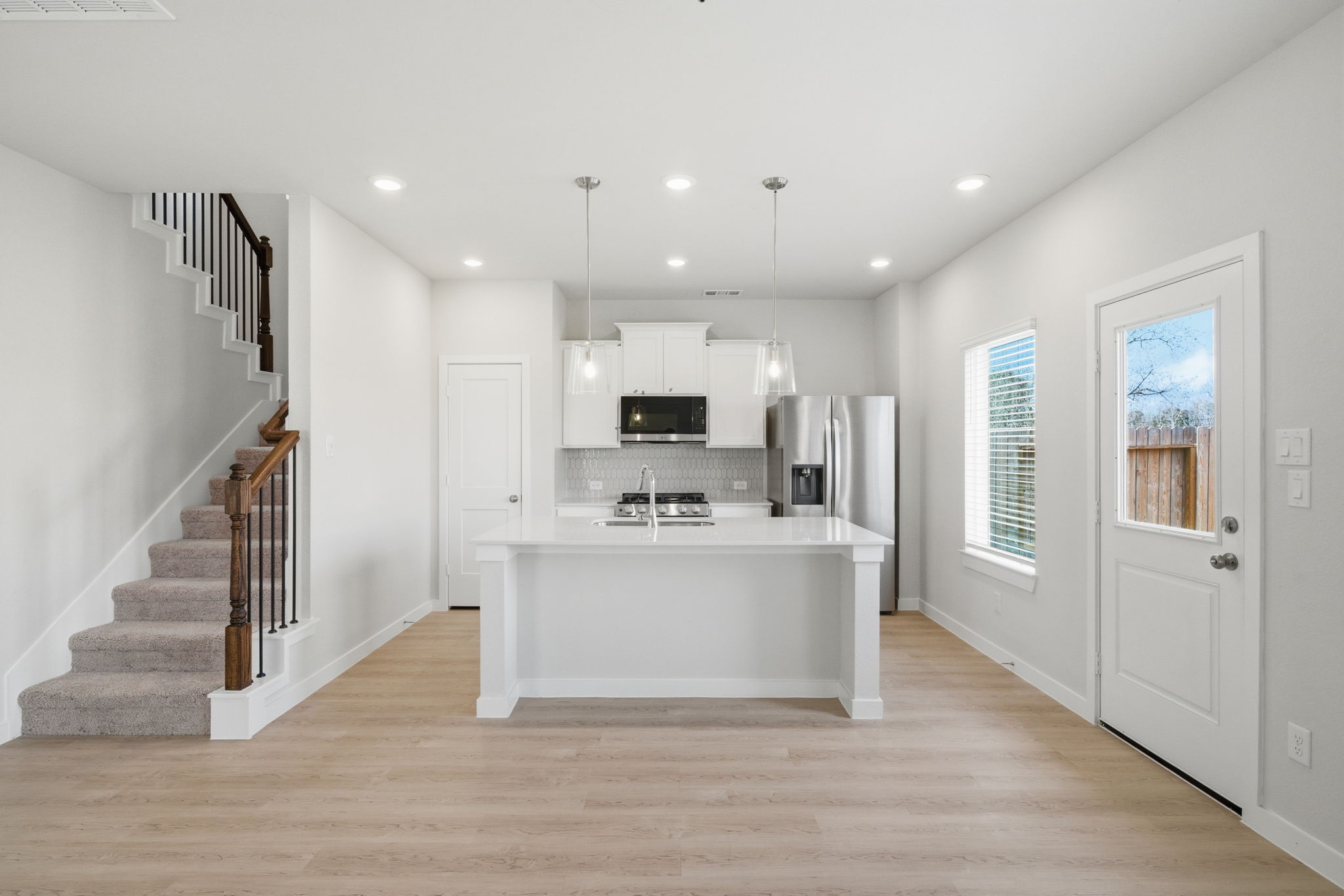 A large kitchen with a large white counter and a white staircase.