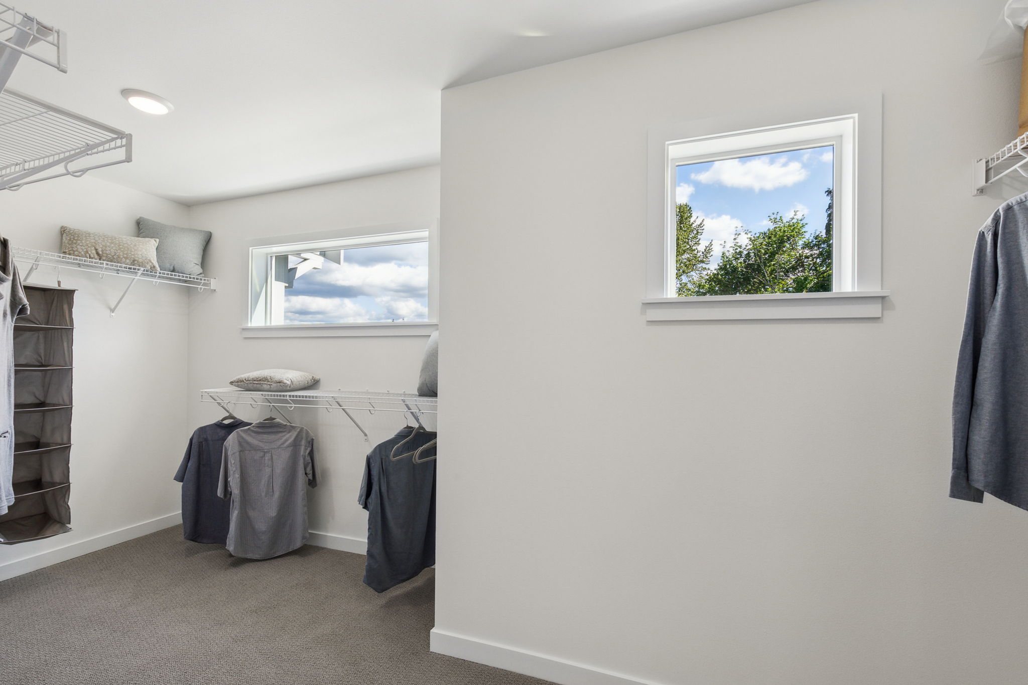 A room with a window and clothes on the wall.